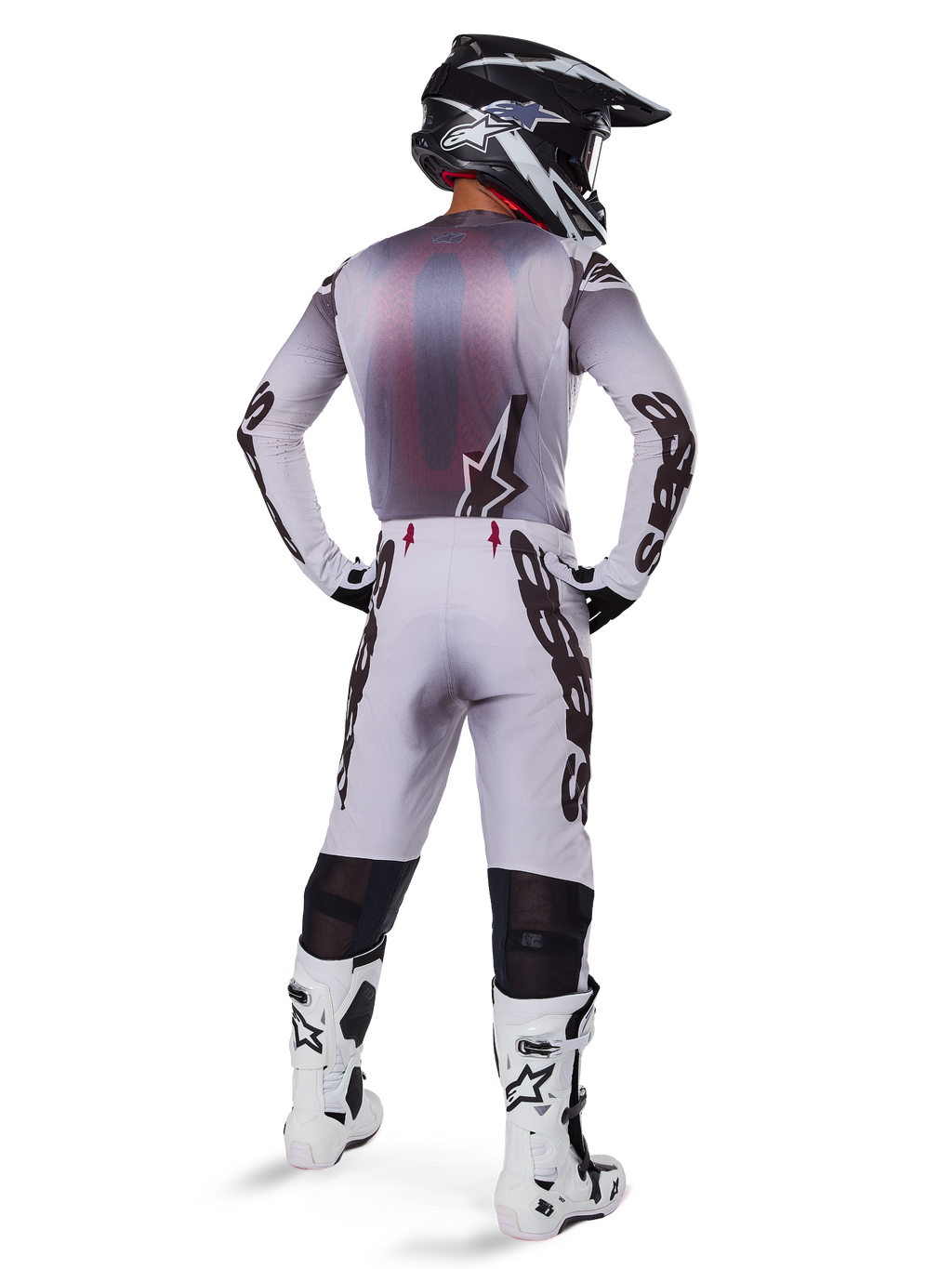 Motorcrosser van achteren gezien in Alpinestars 2025 Supertech Maker broek in zilver en zwart, bijpassende jersey met lange mouwen, zwart-witte helm en wit-zwarte laarzen, met opvallende zwarte branding op de benen, professionele off-road race-uitrusting.