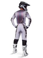 Alpinestars motorcrossrijder in volledige race-uitrusting, grijs en zwart shirt, lichtgrijze broek met zwarte 'Astars' branding aan de zijkanten, zwart-witte helm, witte Tech 10 laarzen, gecoördineerde professionele off-road race-outfit