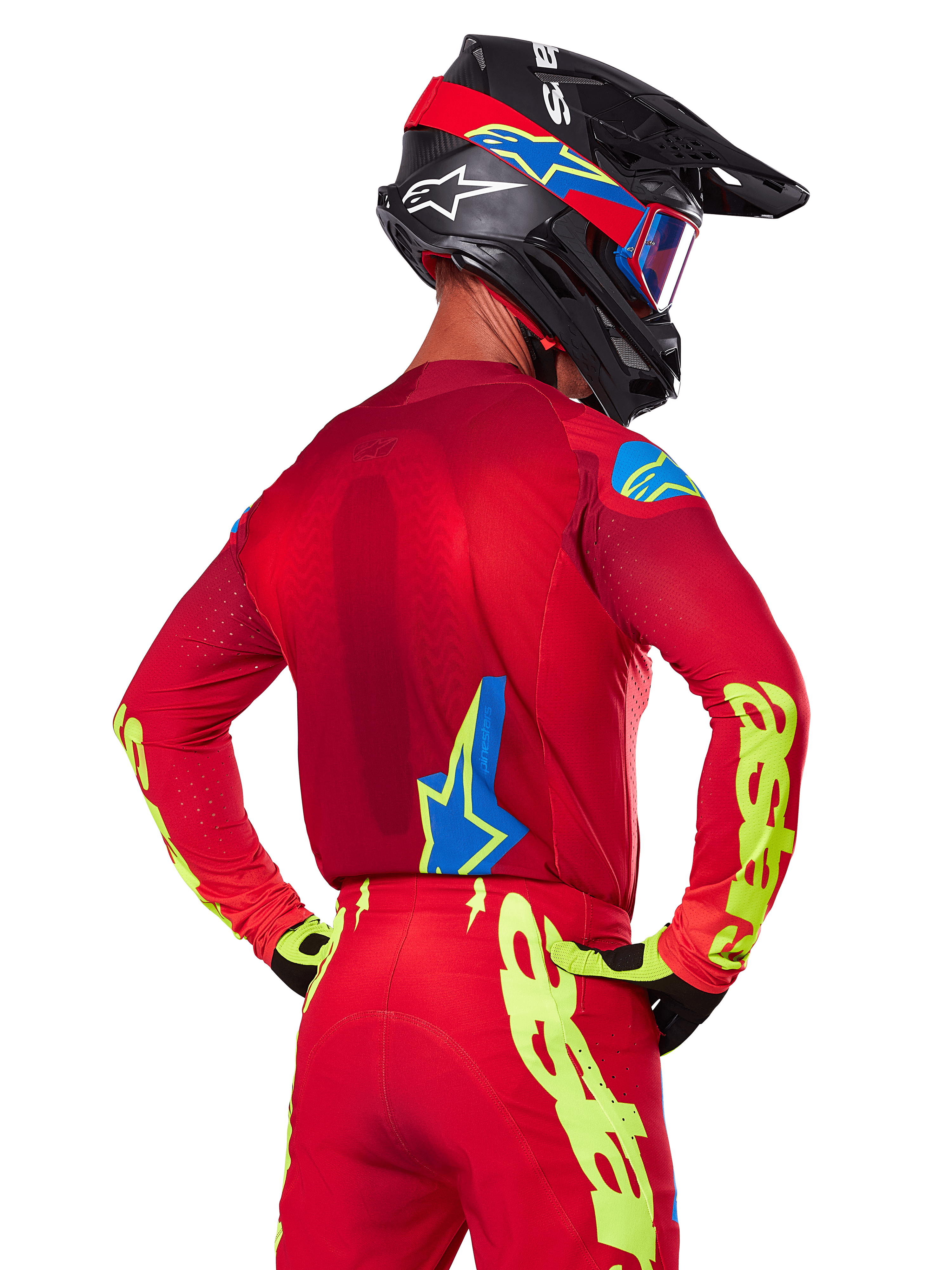 Achteraanzicht van een motocrossrijder die de Alpinestars 2025 Supertech Maker Gear Set in het rood draagt, bestaande uit een rode jersey met neongele branding op de mouwen, een bijpassende rode broek, een zwarte helm met blauwe en rode accenten en bijpassende zwart-gele handschoenen.