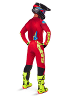 Motocrossrijder van achteren gezien in de Alpinestars 2025 Supertech Maker Gear Set, helderrood jersey met fluogele branding, bijpassende rode broek met gele accenten, zwarte helm met rode en blauwe details, fluogele laarzen, gecoördineerde professionele race-outfit voor off-road prestaties.