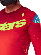 Alpinestars 2025 Supertech Maker Jersey, motocross jersey, felrood en fluoriserend geel, close-up weergave met lasergesneden perforaties, geel Alpinestars-logo op de borst, blauw schouderdetail, ademende stretch mesh-stof
