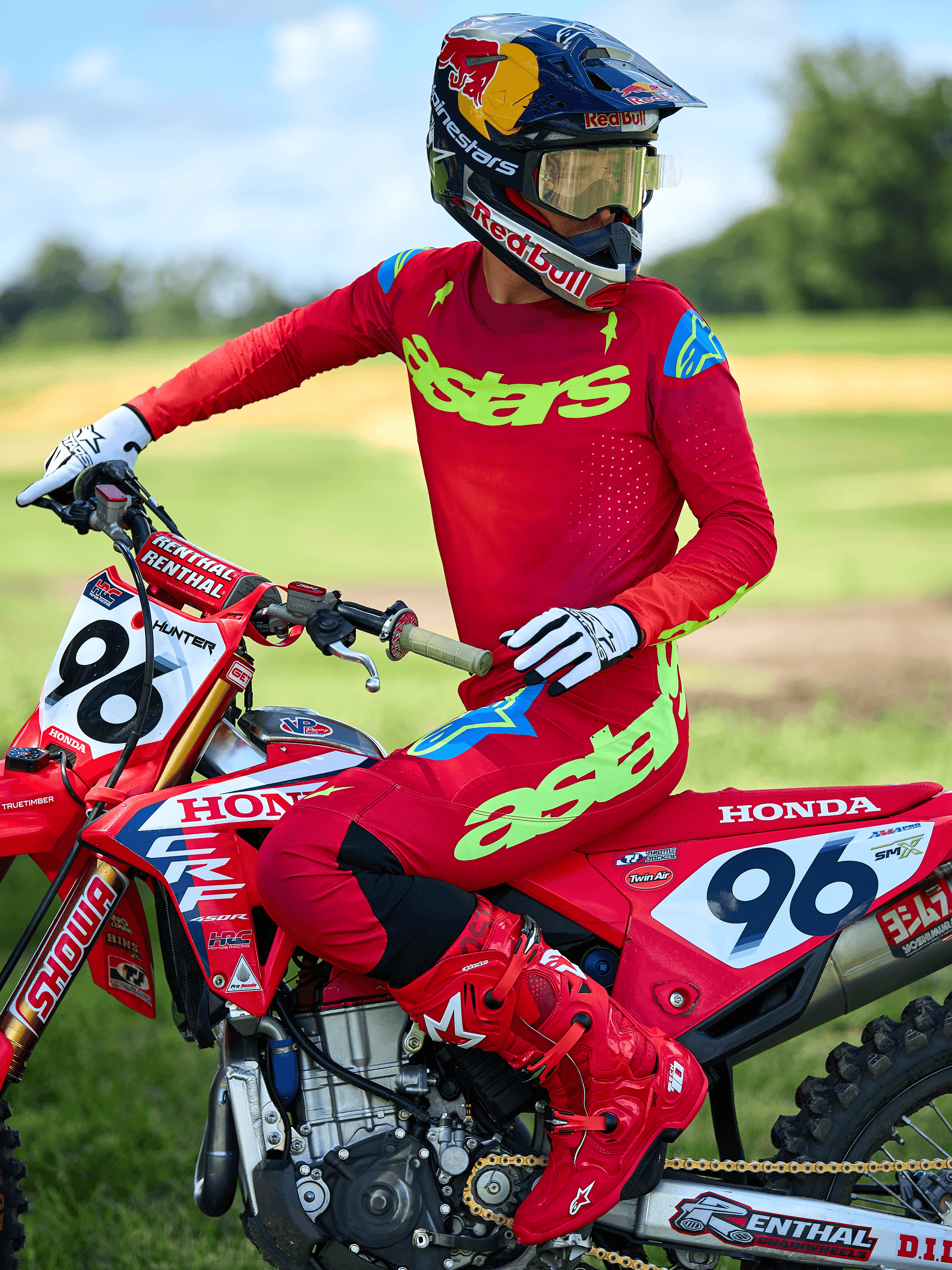 Motocross rider wearing the Alpinestars 2025 Supertech Maker Jersey, Bright Red with Neon Yellow 'astars' branding, worn with matching red pants and boots, white and black gloves, sitting on a red Honda racing bike in an outdoor setting