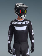 Alpinestars 2026 Racer Air Riway Jersey, zwart-wit motorcross jersey met 'astars' branding, gedragen door een rijder met bijpassende zwarte helm, crossbril en broek, voorzien van ademende mesh-panelen voor off-road racen.