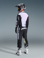 Motorcrosser van achteren gezien in de 2026 Racer Air Riway Jersey in zwart en wit, met het grote witte mesh rugpaneel voor luchtstroom, gecombineerd met een zwarte broek, zwart-witte helm en witte racelaarzen, complete professionele uitrusting voor off-road prestaties.