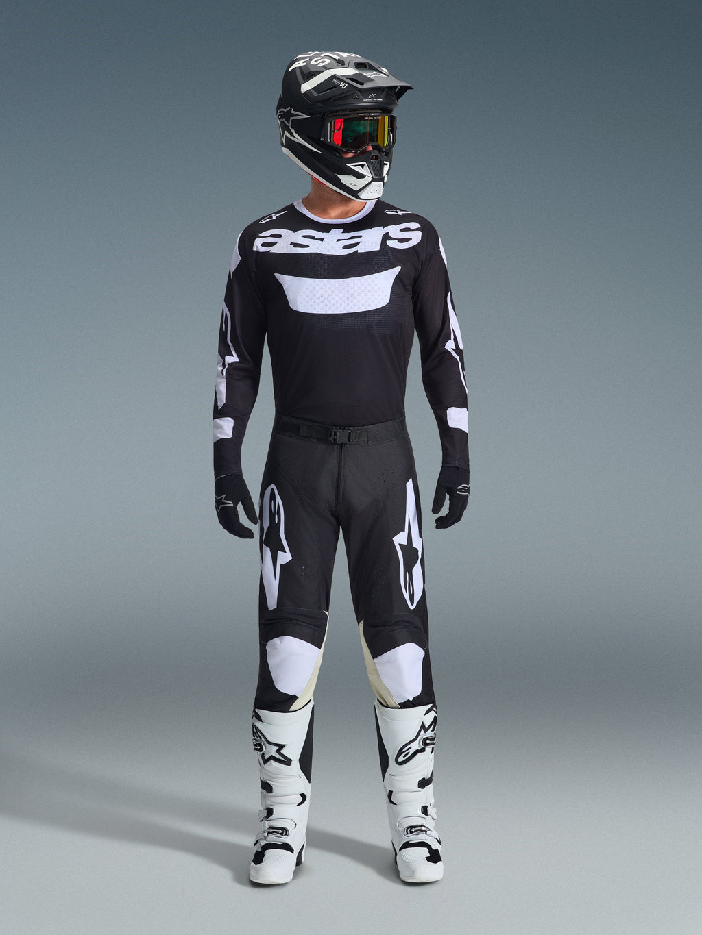 Alpinestars 2026 Racer Air Riway Jersey in zwart en wit, motorcrosser in volledige uitrusting, 'astars' branding op de borst, bijpassende zwarte broek met witte accenten, witte motorcrosslaarzen en zwart-witte helm met bril, gecoördineerde professionele off-road race-outfit