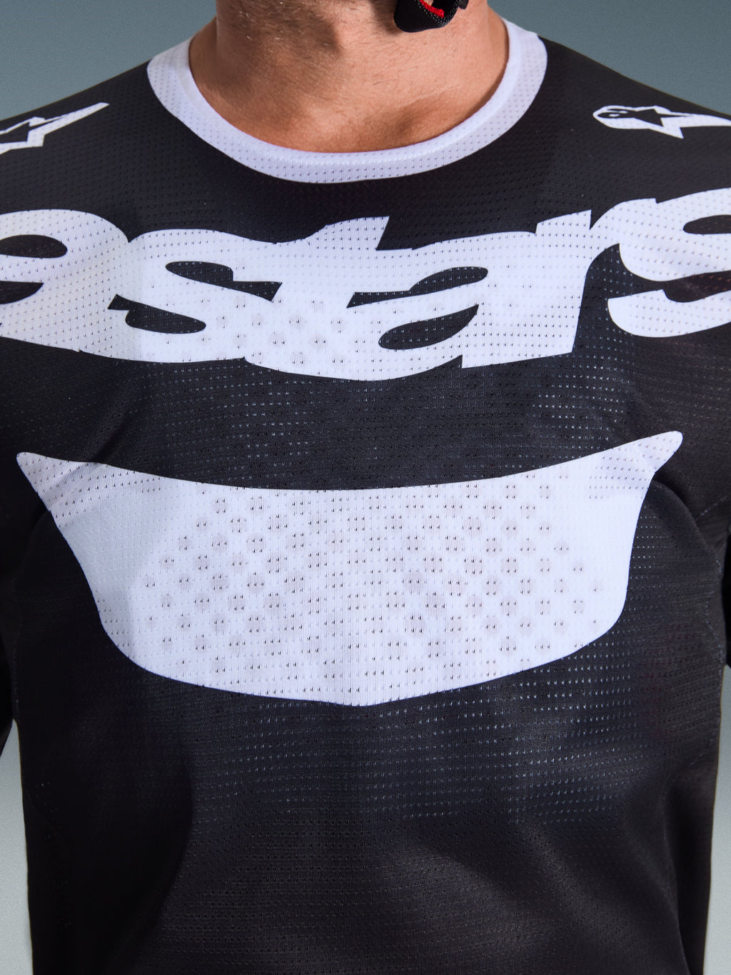 Alpinestars 2026 Racer Air Riway Jersey, motorcross shirt, zwart en wit, close-up van de borst met groot wit logo, gedetailleerde mesh-textuur voor luchtstroom, technische ademende uitrusting voor off-road rijden