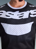 Alpinestars 2026 Racer Air Riway Jersey, motorcross shirt, zwart en wit, close-up van de borst met groot wit logo, gedetailleerde mesh-textuur voor luchtstroom, technische ademende uitrusting voor off-road rijden