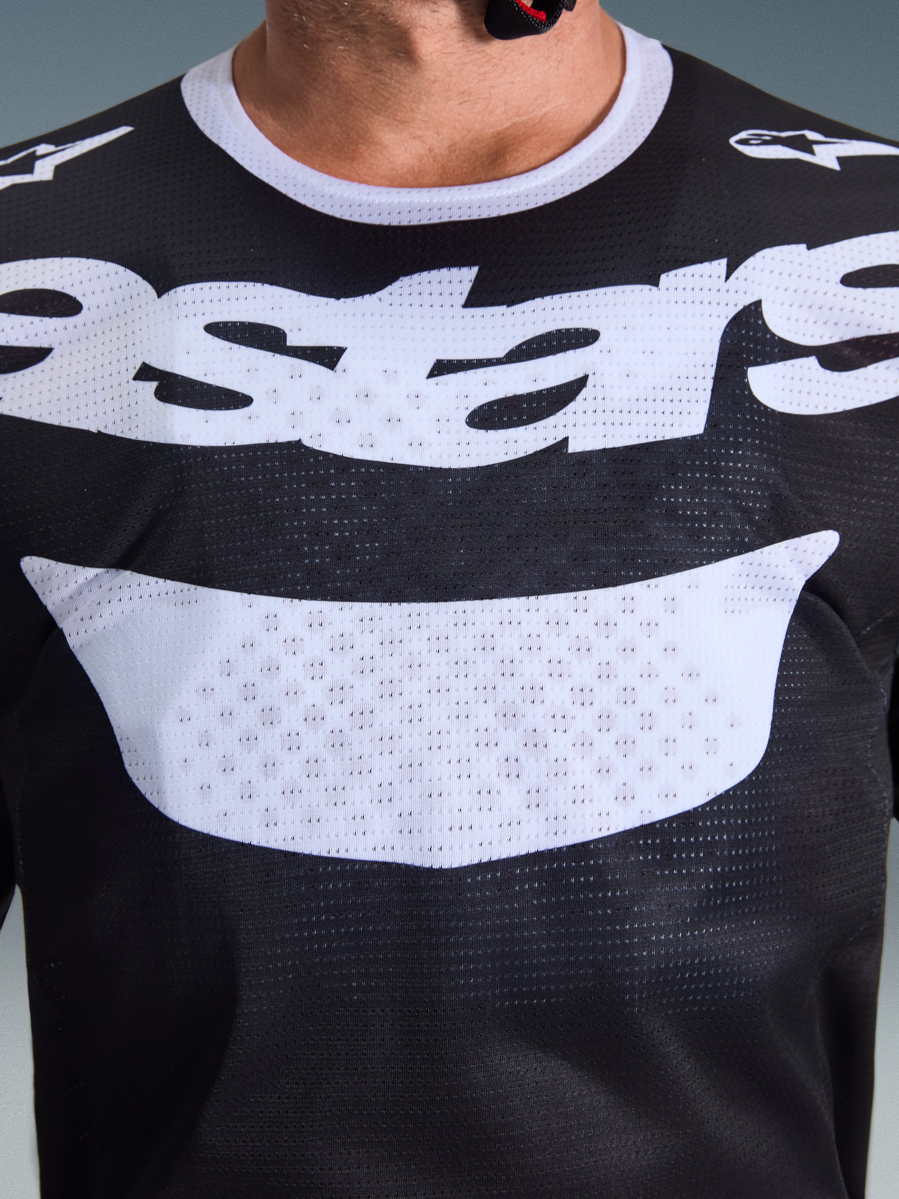 Alpinestars 2026 Racer Air Riway Jersey, motorcross shirt, zwart en wit, close-up van de borst met groot wit logo, gedetailleerde mesh-textuur voor luchtstroom, technische ademende uitrusting voor off-road rijden