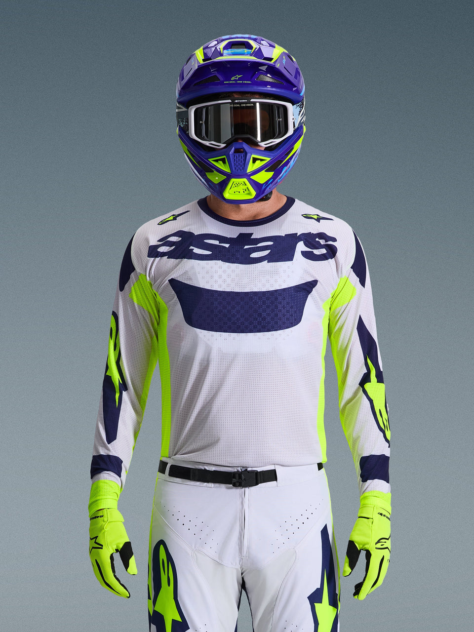 Alpinestars 2026 Racer Air Riway Jersey, lichtgrijs met donkerblauw astars-logo, fluoriserend gele en blauwe accenten op de mouwen, gedragen door een motorcrosser met bijpassende paarse en neongele helm en handschoenen, technische mesh-stof voor off-road racing