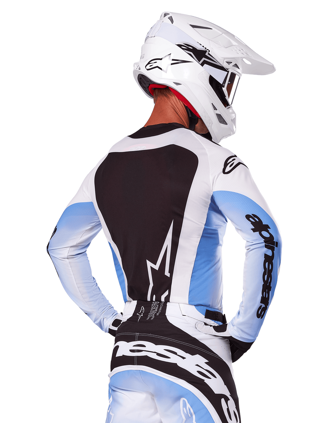 Achteraanzicht van een motorcrossrijder in de Alpinestars 2025 Techstar Melt Gear Set in wit en blauw, jersey met een groot zwart rugpaneel en wit sterlogo, mouwen met lichtblauw kleurverloop, bijpassende wit-blauwe broek, witte racehelm en zwart-witte handschoenen, gecoördineerde performance-uitrusting voor motorcross