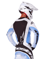 Achteraanzicht van een motorcrossrijder in de Alpinestars 2025 Techstar Melt Gear Set in wit en blauw, jersey met een groot zwart rugpaneel en wit sterlogo, mouwen met lichtblauw kleurverloop, bijpassende wit-blauwe broek, witte racehelm en zwart-witte handschoenen, gecoördineerde performance-uitrusting voor motorcross