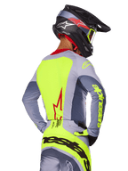 Alpinestars 2025 Techstar Melt Jersey, Bright Red Gray, achteraanzicht van motorcrossrijder in grijze en neongele race-uitrusting, rood sterlogo op de rug, bijpassende zwarte en rode helm, hoogwaardige off-road kleding