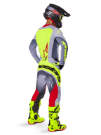 Alpinestars 2025 Techstar Melt Jersey in Bright Red Gray, motocrossrijder van achteren gezien met een felgeel rugpaneel en grijze mouwen, bijpassende grijze en rode broek met gele branding, felgele motorcrosslaarzen en een zwarte helm met gele goggles, complete off-road race-outfit