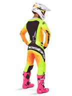 Motorcrosser van achteren die de Alpinestars 2025 Techstar Melt Jersey draagt, opvallend geel en oranje kleurverloop met zwarte delen, bijpassende motorcrossbroek, felroze laarzen en witte helm, atletische pasvorm voor off-road competitie.
