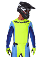 Alpinestars 2025 Techstar Melt Jersey, motorcross racetenue, fluogeel en blauw, voorzien van laser-gesneden ventilatie en een atletische racepasvorm, gedragen door een rijder met een zwarte helm en fluogele handschoenen