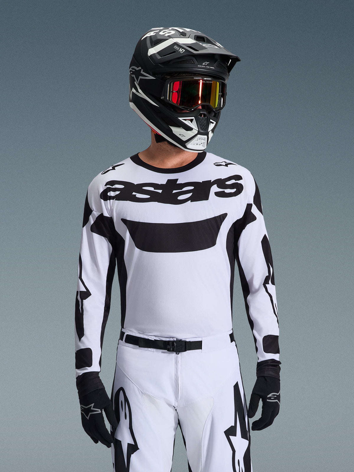 Motocross-rijder in de Alpinestars 2026 Racer Riway Jersey in wit en zwart, voorzien van 'astars'-branding op de borst, gecombineerd met een bijpassende zwart-witte broek, een zwarte helm met bril en zwarte handschoenen, gecoördineerde set voor off-road racen.