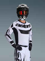 Alpinestars 2026 Racer Riway Jersey, motorcross jersey, wit en zwart, met opvallend 'astars' logo op de borst, gedragen met bijpassende witte broek en zwarte handschoenen, zwart-witte helm met rode reflecterende bril, professionele off-road race-uitrusting