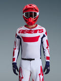 Motocross rider wearing the Alpinestars 2026 Racer Riway Jersey in White Blue Red, featuring a large red 'astars' logo on the chest, navy blue side panels, matching white and red motocross pants, a red helmet with white goggles, and navy blue gloves, complete off-road racing gear set.