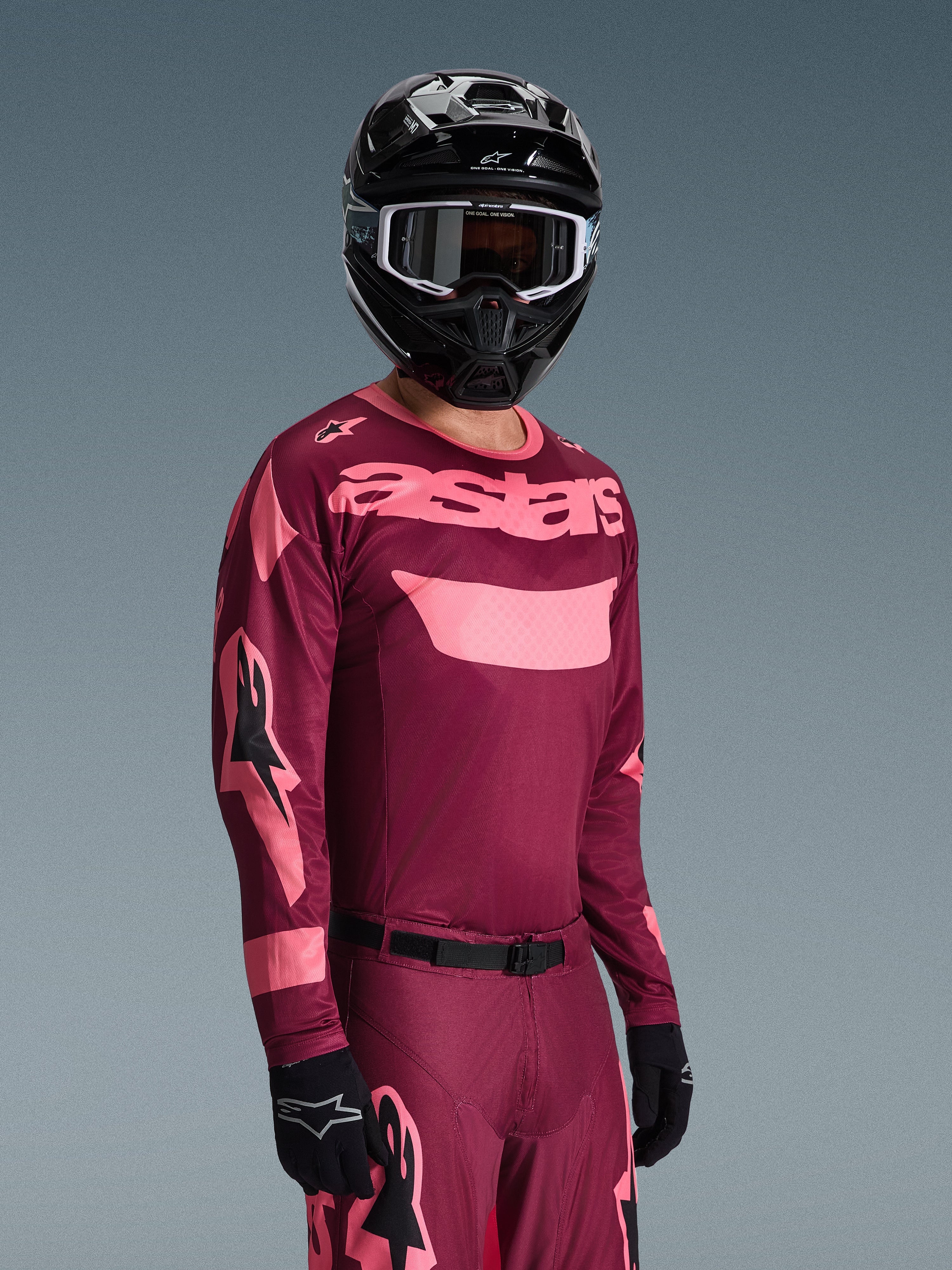 Alpinestars 2026 Racer Riway Gear Set, motocrossrijder met bordeauxrode en roze jersey met opvallende 'astars' branding, bijpassende broek met roze accenten, zwarte helm en handschoenen, professionele race-outfit voor off-road motorcross
