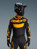 Motorcrossrijder in de Alpinestars 2026 Racer Riway Jersey in geel en zwart, voorzien van een opvallend geel 'astars' logo op de borst, gecombineerd met een bijpassende zwart-gele broek, een zwarte helm met crossbril en zwarte handschoenen, professionele off-road race-uitrusting.