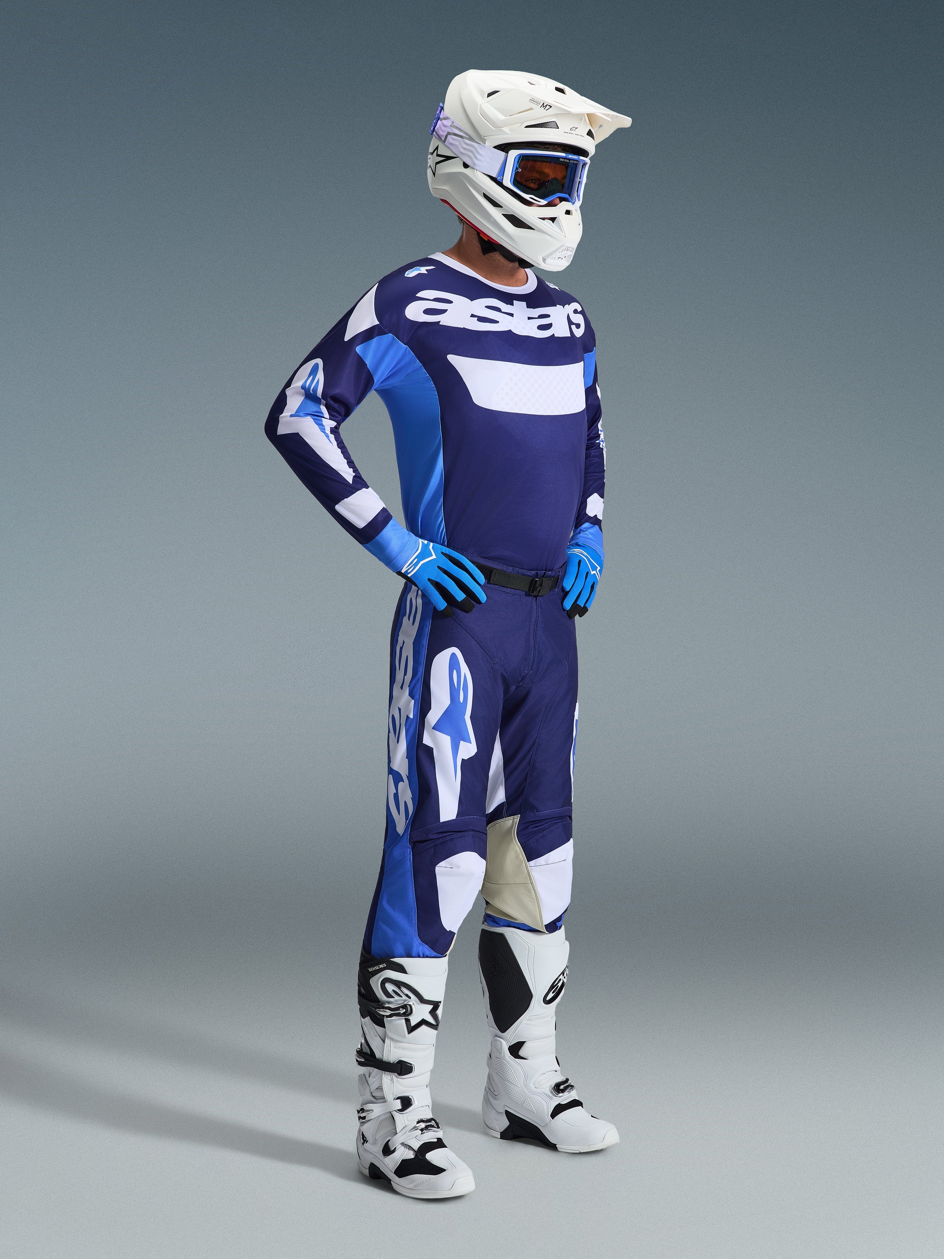 Alpinestars 2026 Racer Riway Jersey in Ucla Blue en wit, gedragen door een motorcrosser met bijpassende broek, witte helm, blauwe handschoenen en witte laarzen, voorzien van opvallende 'astars' branding op de borst, complete off-road race-outfit