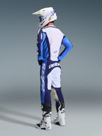 Motorcrossrijder die de 2026 Racer Riway Jersey in Ucla Blue en wit draagt, gecombineerd met een bijpassende blauw-witte crossbroek, witte helm en witte laarzen, driekwart achteraanzicht voor een complete off-road racing-look.