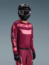 Alpinestars 2026 Racer Riway Jersey in Dark Red Coral met bijpassende broek, voorzien van koraalroze 'astars' branding op de borst, gecombineerd met een zwarte helm en zwarte handschoenen, gecoördineerde motorcross outfit.