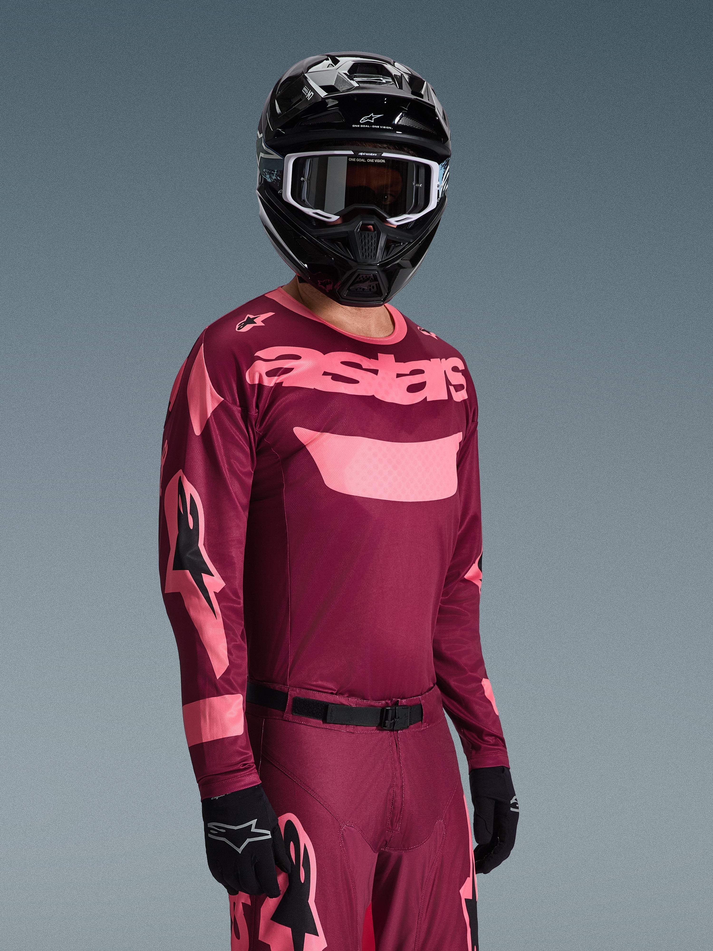 Alpinestars 2026 Racer Riway Jersey in Dark Red Coral met bijpassende broek, voorzien van koraalroze 'astars' branding op de borst, gecombineerd met een zwarte helm en zwarte handschoenen, gecoördineerde motorcross outfit.