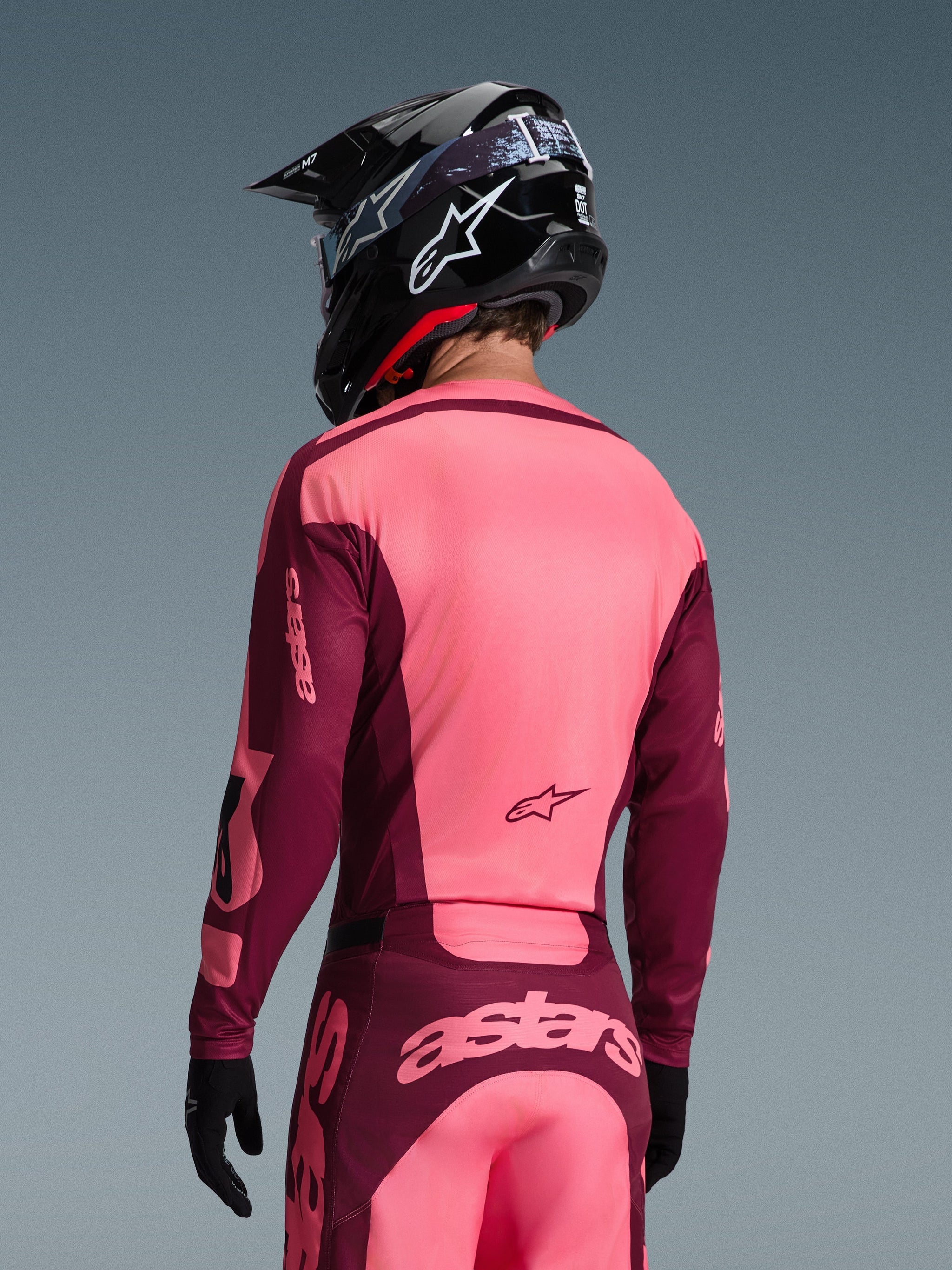 Motocrossrijder van achteren gezien in Alpinestars 2026 Racer Riway Jersey en bijpassende broek, Dark Red en Coral kleurstelling, zwarte helm met wit Alpinestars-logo, zwarte handschoenen, professionele uitrusting voor off-road racing