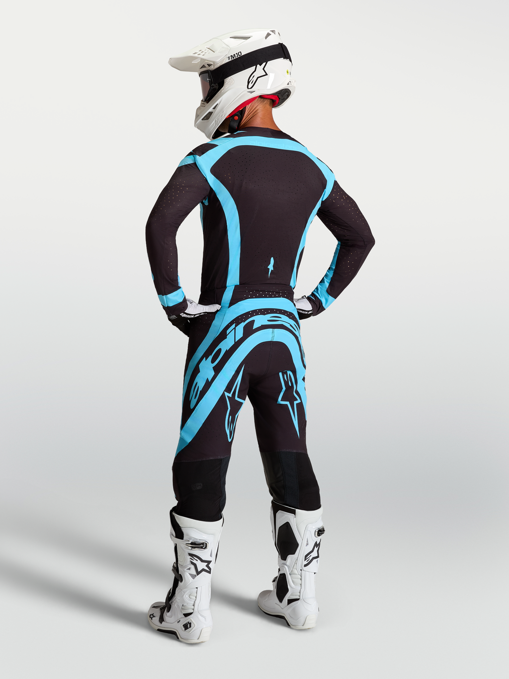 Alpinestars 2027 Supertech Vesta Jersey and Gear Set, black and turquoise motocross outfit with white boots, rear view.