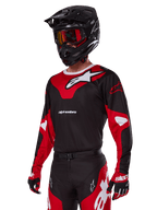 Motorcrosser met Alpinestars 2025 Racer Veil Gear Set, rood en zwart jersey met wit Alpinestars-logo, bijpassende broek en handschoenen, zwarte helm met rode crossbril, technische off-road racekleding