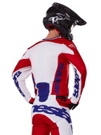Alpinestars 2025 Racer Veil Jersey en broek, motorcross kledingset, helder rood, wit en blauw, achteraanzicht van rijder met bijpassende uitrusting en zwarte motorcrosshelm, voorzien van opvallende blauwe Alpinestars-branding, technische off-road racekleding.
