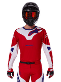 Alpinestars 2025 Racer Veil Jersey, motocross raceshirt, rood, wit en blauw, lange mouwen, gedragen met zwarte helm en oranje bril, bijpassende rode handschoenen en broek, gestroomlijnd ontwerp voor off-road prestaties