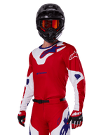 Alpinestars 2025 Racer Veil Gear Set, motocrossrijder met rood, wit en blauw raceshirt en broek, zwarte helm met oranje gespiegelde crossbril, rood-witte handschoenen, technische off-road uitrusting met opvallende branding