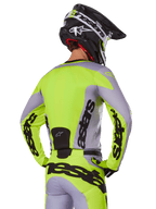 Alpinestars 2025 Racer Veil Jersey in Gray Yellow Fluo, motocross jersey van achteren gezien, met opvallende 'astars' branding op de rug en mouwen, gecombineerd met bijpassende broek en zwarte helm voor een complete race-look.