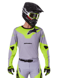 Alpinestars 2025 Racer Veil Jersey, motorcross shirt met lange mouwen, grijs en neongeel met zwarte Alpinestars-logo's, getoond als onderdeel van een complete race-uitrusting met bijpassende broek, zwarte helm en handschoenen