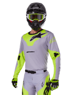 Motorcrosser met Alpinestars 2025 Racer Veil Gear Set in grijs en fluogroen, lichtgrijze jersey en broek met opvallende neongele panelen en zwarte Alpinestars-logo's, bijpassende handschoenen en een zwarte helm met neongroene bril, professionele off-road racekleding
