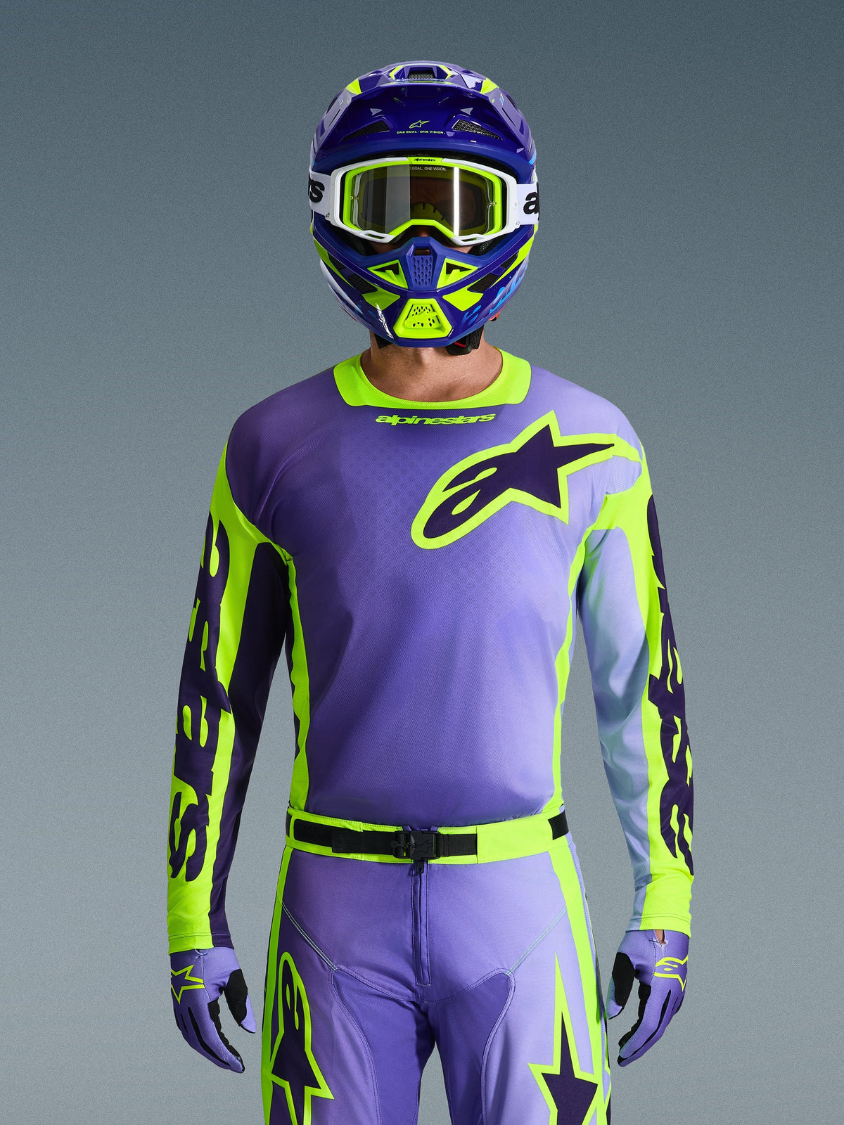Alpinestars 2026 Racer Portl Jersey, motorcross jersey, paars en fluoriserend geel, gedragen met bijpassende motorcrossbroek, handschoenen en helm, voorzien van een groot Alpinestars sterlogo op de borst, studio-opname tegen een grijze achtergrond.