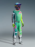 Motocross rider wearing complete racing gear, 2026 Racer Portl Jersey in green with white and black sleeves and pink logo, matching green pants with pink accents, multi-colored helmet with goggles, white and black boots, and green gloves, coordinated outfit for off-road racing