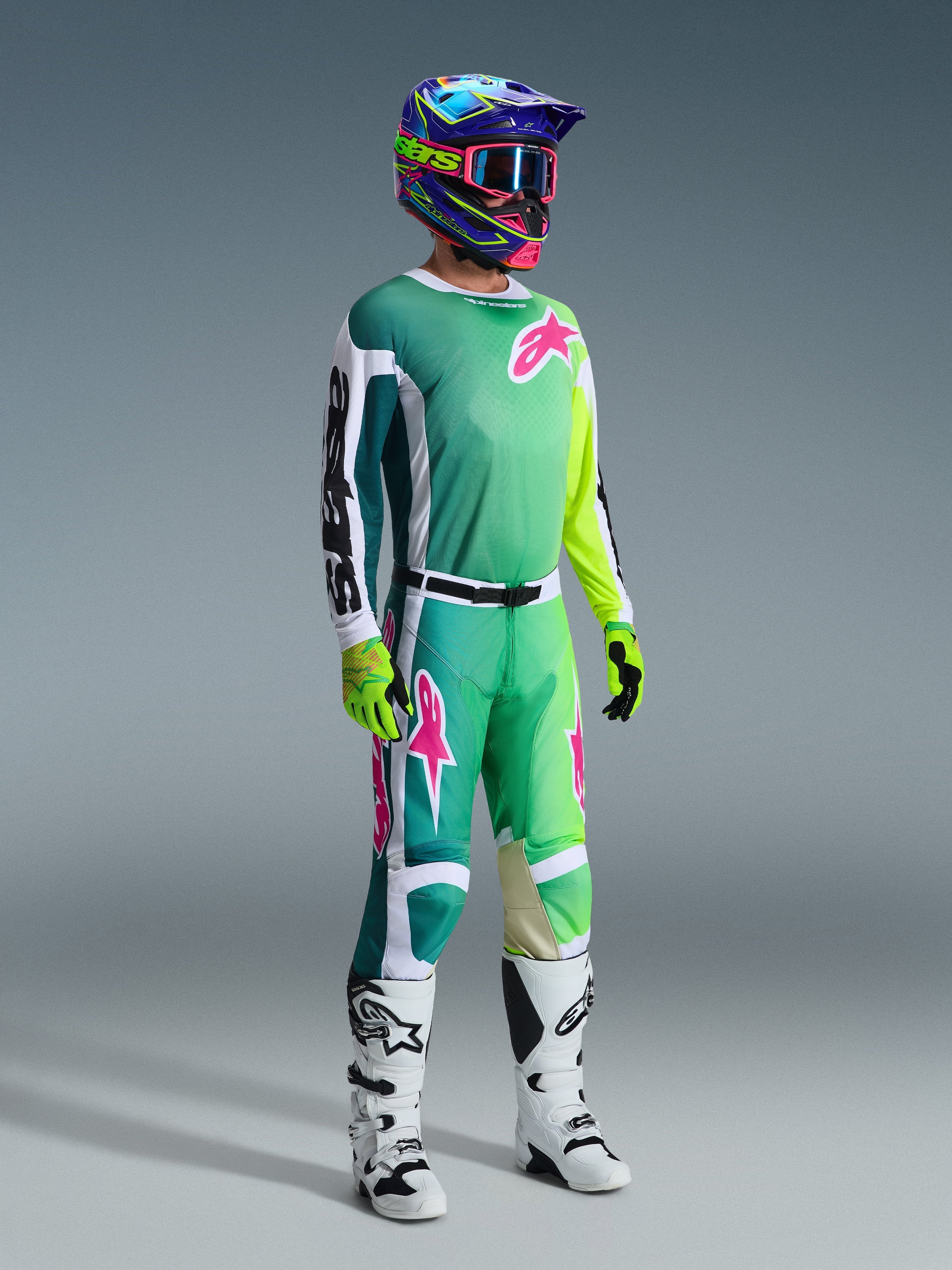 Motocross rider wearing complete racing gear, 2026 Racer Portl Jersey in green with white and black sleeves and pink logo, matching green pants with pink accents, multi-colored helmet with goggles, white and black boots, and green gloves, coordinated outfit for off-road racing