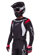 Alpinestars 2025 Fluid Haul Gear Set, motorcross outfit, zwarte jersey met rode schouderpanelen en witte graphics, bijpassende zwarte broek met witte ster-logo's, rode en zwarte handschoenen, zwarte helm met witte accenten en bril, gecoördineerde motorcrossuitrusting