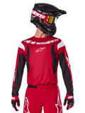 Alpinestars 2025 Fluid Haul Jersey, motorcross shirt, felrood en zwart, gedragen als onderdeel van een volledige set met bijpassende broek en handschoenen, zwarte helm met crossbril met gele lens, witte merklogo's, hoogwaardige off-road racekleding