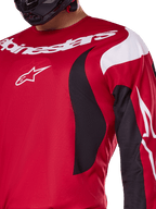 Alpinestars 2025 Fluid Haul Jersey, helder rood en zwart, close-up van de borst en arm met witte Alpinestars-branding en logo, atletisch ergonomisch ontwerp met zwarte en witte golvende accenten voor motorcross-prestaties.