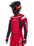 Alpinestars 2025 Fluid Haul Gear Set in het rood, motorcrossrijder in rode jersey met witte en zwarte accenten, bijpassende rode broek met witte graphics, zwarte helm met witte branding, rood-gele crossbril en rood-zwarte handschoenen, gecoördineerde motorcross race-outfit