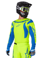 Alpinestars 2025 Fluid Haul gearset, motorcross jersey en broek, felgeel en blauw, gedragen met een zwarte helm en crossbril met geel montuur, voorzien van blauwe golfpatronen op de mouwen en blauwe sterlogo's op de broek, bijpassende off-road race-outfit