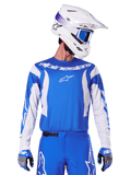 Alpinestars 2025 Fluid Haul Jersey, motorcross jersey, blauw en wit, gedragen met bijpassende broek en handschoenen, witte helm met blauwe crossbril, gecoördineerde MX-uitrusting voor off-road rijden