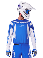 Alpinestars 2025 Fluid Haul Jersey, motorcross jersey, blauw en wit, gedragen met bijpassende broek en handschoenen, witte helm met blauwe crossbril, gecoördineerde MX-uitrusting voor off-road rijden