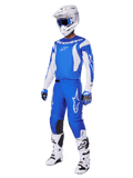 Motorcrosser die de volledige 2025 Fluid Haul Gear Set draagt, blauwe en witte jersey en broek met Alpinestars-branding, witte helm met blauwe bril, witte laarzen en blauwe handschoenen, gecoördineerde race-outfit voor off-road motorcross.