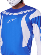 Alpinestars 2025 Fluid Haul Jersey, blauw en wit, gedragen door een rijder met een witte helm, voorzien van een wit Alpinestars-woordmerk en A-star logo, atletische pasvorm, lichtgewicht vochtafvoerend materiaal voor motorcross en off-road rijden