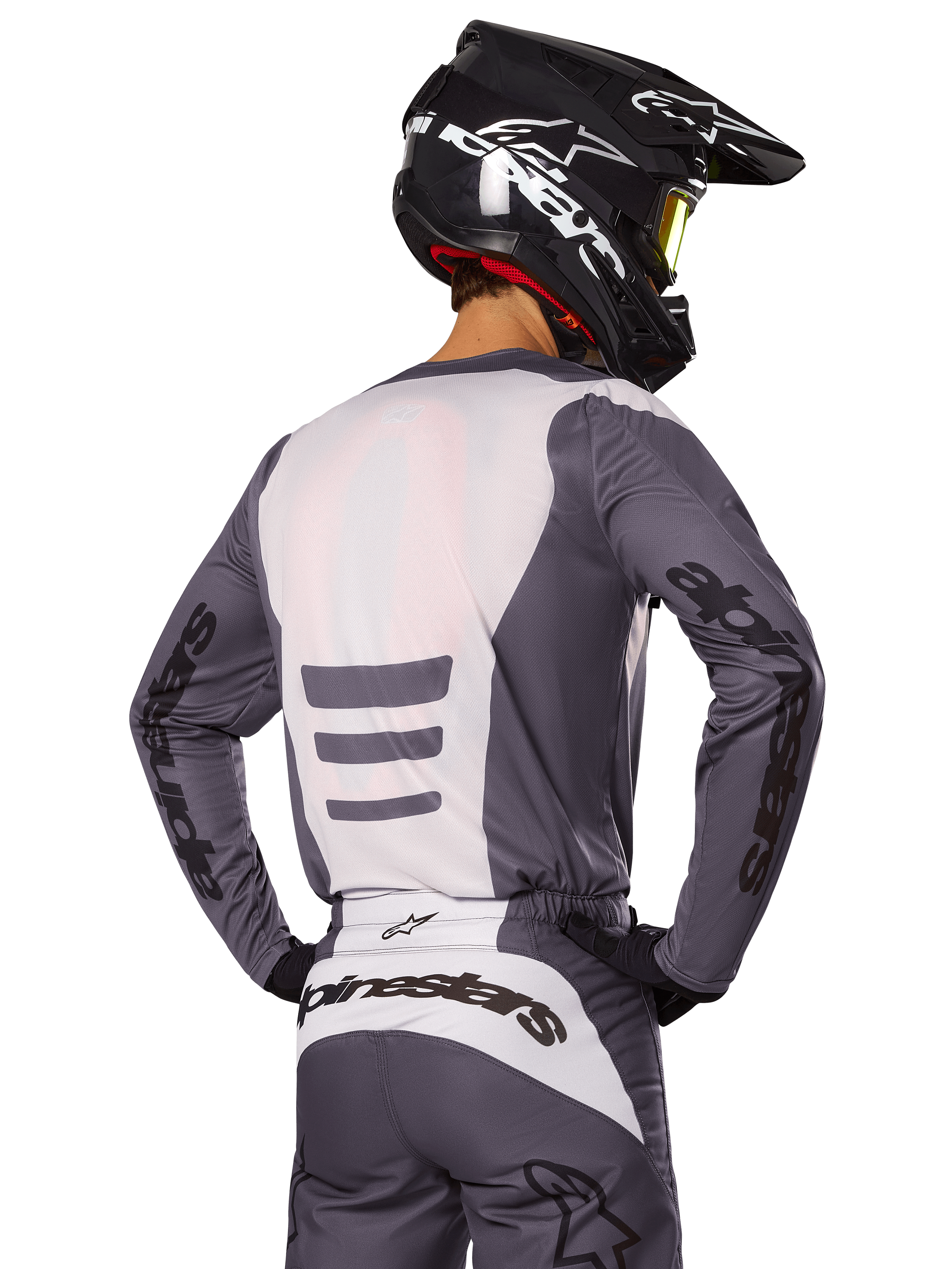 Motocrossrijder van achteren die de Alpinestars 2025 Fluid Haul Gear Set draagt, grijs en witte jersey en broek, zwarte helm met witte graphics, gele goggle, gecoördineerde motorcross race-outfit